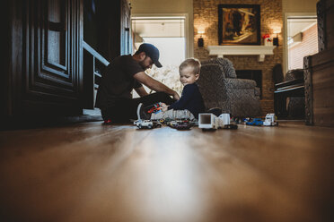 Surface level image of father and son playing with toy cars on floor at home - CAVF50097