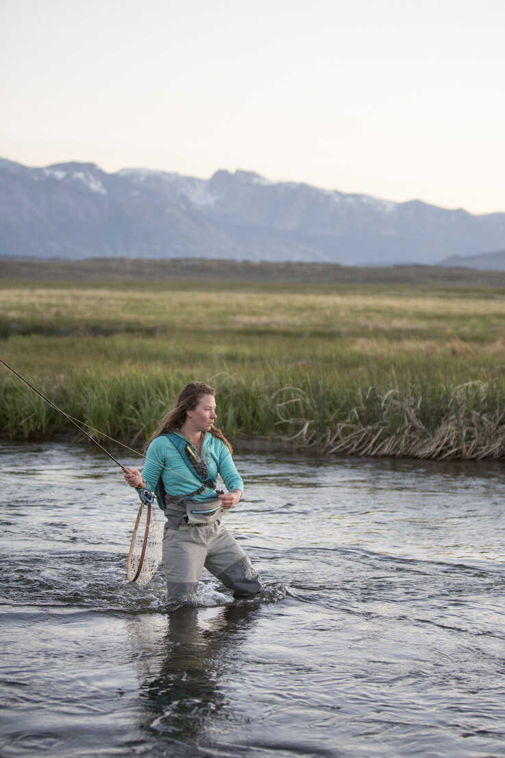 Young woman fly-fishing while standing in Owens River against mountains  stock photo