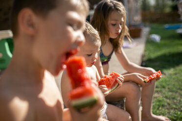 Geschwister essen Wassermelonen, während sie im Garten sitzen - CAVF50120
