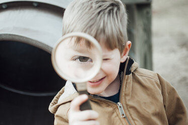Close-up portrait of happy boy playing with magnifying glass at playground - CAVF50122