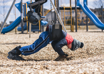 Seitenansicht eines Jungen beim Schaukeln auf dem Spielplatz - CAVF50123