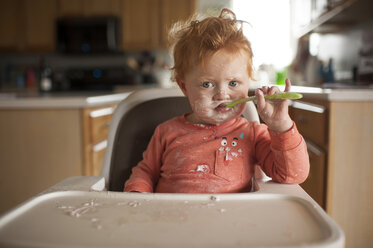 Porträt der niedlichen Baby-Junge mit unordentlichen Gesicht Essen zu essen, während auf Hochstuhl zu Hause sitzen - CAVF50177