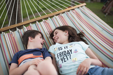 Hoher Blickwinkel auf glückliche Geschwister, die sich auf einer Hängematte im Garten entspannen - CAVF50180
