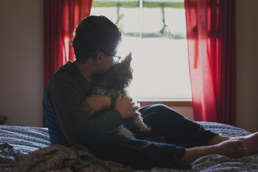 Boy embracing dog while sitting on bed at home - CAVF50188