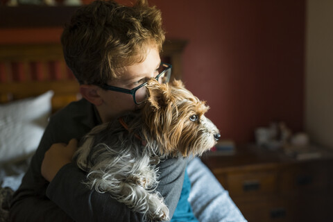 Junge mit Hund, der wegschaut, während er zu Hause auf dem Bett sitzt, lizenzfreies Stockfoto