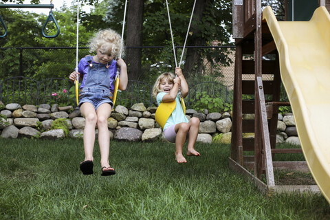 Glückliche süße Schwestern schaukeln auf dem Spielplatz, lizenzfreies Stockfoto