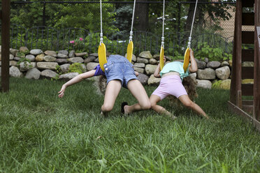 Happy playful sisters lying on swings at playground - CAVF50207