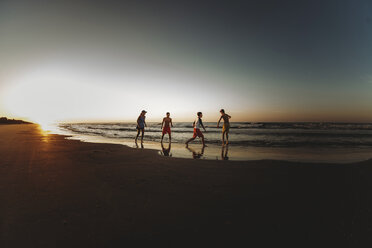 Glückliche Geschwister spielen am Strand gegen den Himmel bei Sonnenuntergang - CAVF50210