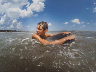 Shirtless teenage boy looking away while surfing on sea against blue sky - CAVF50211