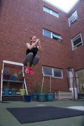 Low angle view of confident woman jumping against building - CAVF50213