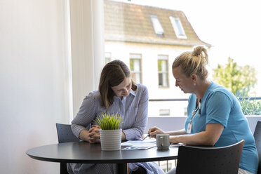 Doctor explaining medical records to female patient while sitting in clinic - CAVF50214