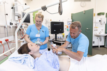 Ärzte untersuchen eine Patientin, die auf einem Bett im Krankenhaus liegt - CAVF50219