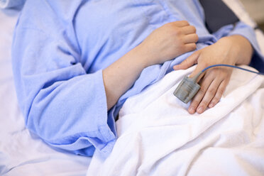 Mittelteil einer Patientin mit Pulsoxymeter auf dem Bett liegend im Krankenhaus - CAVF50220