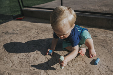 Hoher Blickwinkel des kleinen Jungen, der Kreiden hält, während er auf dem Fußweg auf dem Spielplatz sitzt - CAVF50230