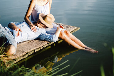 Boyfriend relaxing on girlfriend's lap by lake at park - CAVF50243
