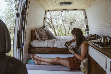 Side view of woman reading book while sitting on seat in motor home - CAVF50257