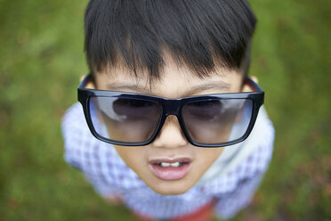 High angle view of boy wearing oversized black sunglasses while standing on field at park - CAVF50275