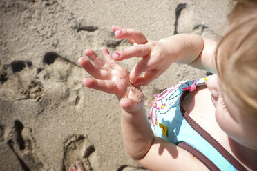 High angle view of girl removing sand from her wet hand at beach during summer - CAVF50296