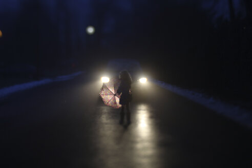 Silhouette Mädchen mit Regenschirm stehend bei Auto auf Straße im Winter bei Nacht - CAVF50297