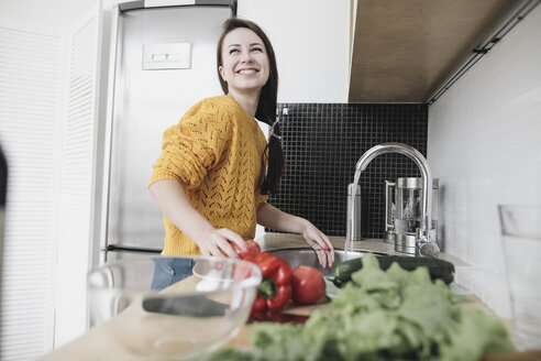 Porträt einer glücklichen jungen Frau, die in einer modernen Küche einen Salat zubereitet - KMKF00573