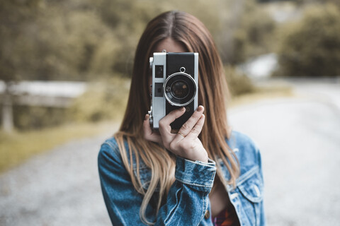 Nahaufnahme einer fotografierenden Frau, die auf der Straße vor Bäumen steht, lizenzfreies Stockfoto