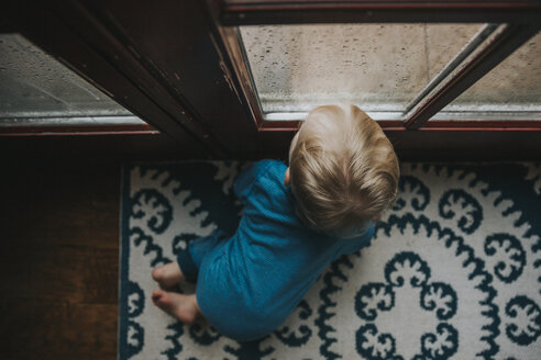Hoher Blickwinkel eines kleinen Jungen, der durch ein nasses Fenster zu Hause schaut - CAVF50311