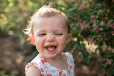 Nahaufnahme eines glücklichen kleinen Mädchens, das im Park vor Pflanzen steht - CAVF50323
