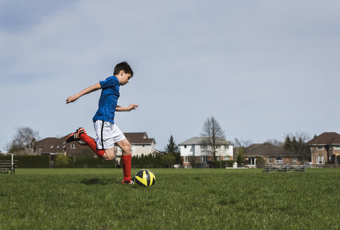 Side view of boy kicking soccer ball while playing on grassy field - CAVF50325