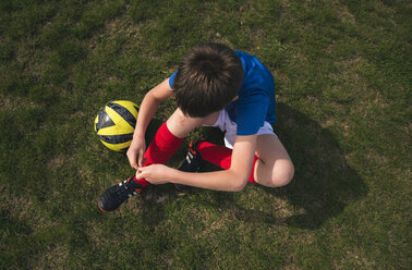 High angle view of boy tying shoelace while sitting on soccer field - CAVF50328