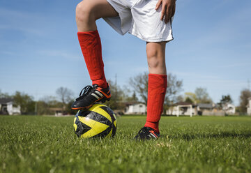 Low section of boy with soccer ball standing on grassy field against sky - CAVF50330