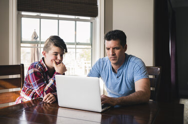 Son looking at father using laptop computer at home - CAVF50342