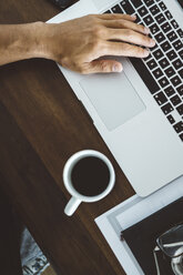 Abgeschnittene Hand eines Mannes mit Kaffeetasse auf dem Tisch, der einen Laptop zu Hause benutzt - CAVF50358