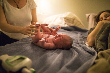 Midwife examining newborn baby girl while mother lying on bed at home - CAVF50368