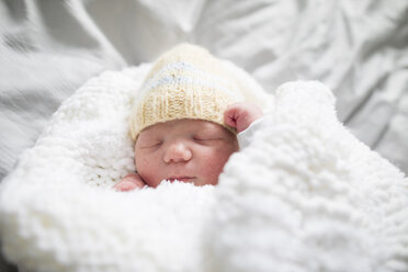Nahaufnahme eines niedlichen neugeborenen Baby-Mädchens mit Strickmütze, das zu Hause auf dem Bett schläft - CAVF50376
