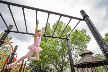 Niedriger Winkel Blick auf niedliche Mädchen in Ballett-Kostüm hängen auf Affenbarren gegen bewölkten Himmel auf dem Spielplatz - CAVF50387