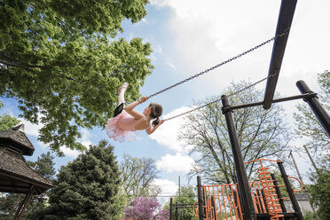 Niedriger Blickwinkel von Mädchen in Ballettkostüm schwingen gegen bewölkten Himmel auf dem Spielplatz - CAVF50389