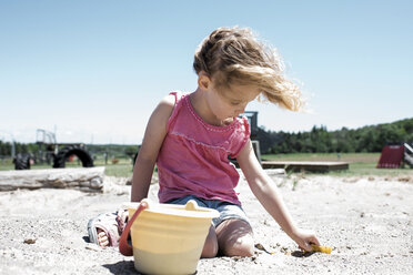 Mädchen spielt mit Sand und kniet vor einem klaren Himmel auf einem Spielplatz an einem sonnigen Tag - CAVF50404