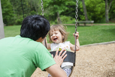 Rückansicht eines Vaters, der seine Tochter auf dem Spielplatz schaukeln lässt - CAVF50406