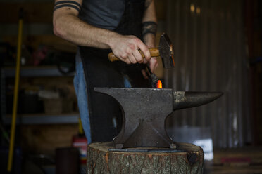 Mittelteil eines Schmieds, der ein Messer auf einem Amboss in einer Werkstatt schmiedet - CAVF50411