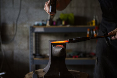 Ausgeschnittenes Bild eines Schmieds, der ein Messer auf einem Amboss in einer Werkstatt schmiedet - CAVF50412