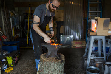 Ein Schmied schmiedet ein Messer auf einem Amboss mit einem Hammer in einer Werkstatt - CAVF50414