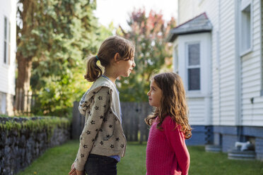 Side view of sisters looking at each other while standing in backyard - CAVF50427