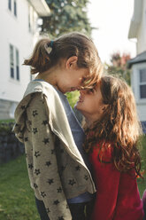 Side view of playful sisters rubbing noses while standing in backyard - CAVF50428