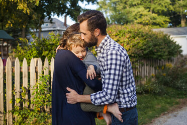 Side view of parents embracing and kissing son while standing against plants in yard - CAVF50436