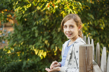 Porträt eines Mädchens, das am Zaun vor Bäumen im Hof steht - CAVF50438