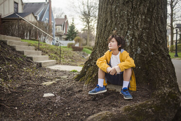 Nachdenklicher Junge, der an einem Baumstamm sitzt und wegschaut - CAVF50439