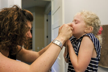 Seitenansicht der Mutter beim Entfernen der Zähne ihrer Tochter zu Hause - CAVF50449