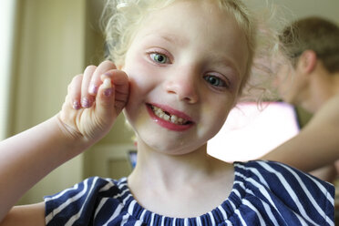 Nahaufnahme eines lächelnden Mädchens, das seine verlorenen Milchzähne zeigt, während es seinem Vater zu Hause gegenübersteht - CAVF50450