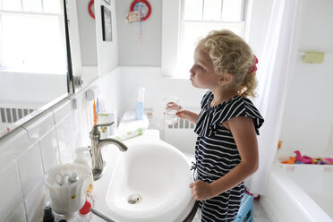 Seitenansicht eines Mädchens, das sich den Mund wäscht und in den Spiegel im Badezimmer schaut - CAVF50451