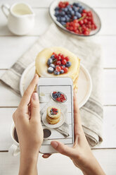 Cropped hands of woman photographing breakfast served on wooden table at home - CAVF50462